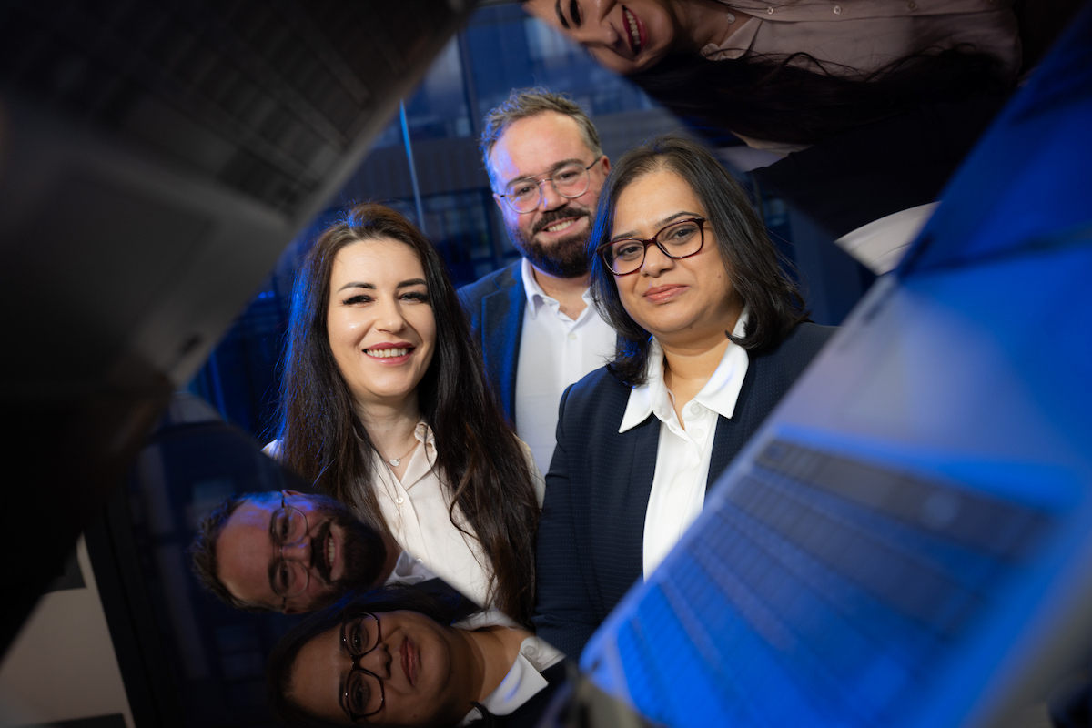 Group of bank of ireland data skills graduates gathered around a laptop in a modern office setting