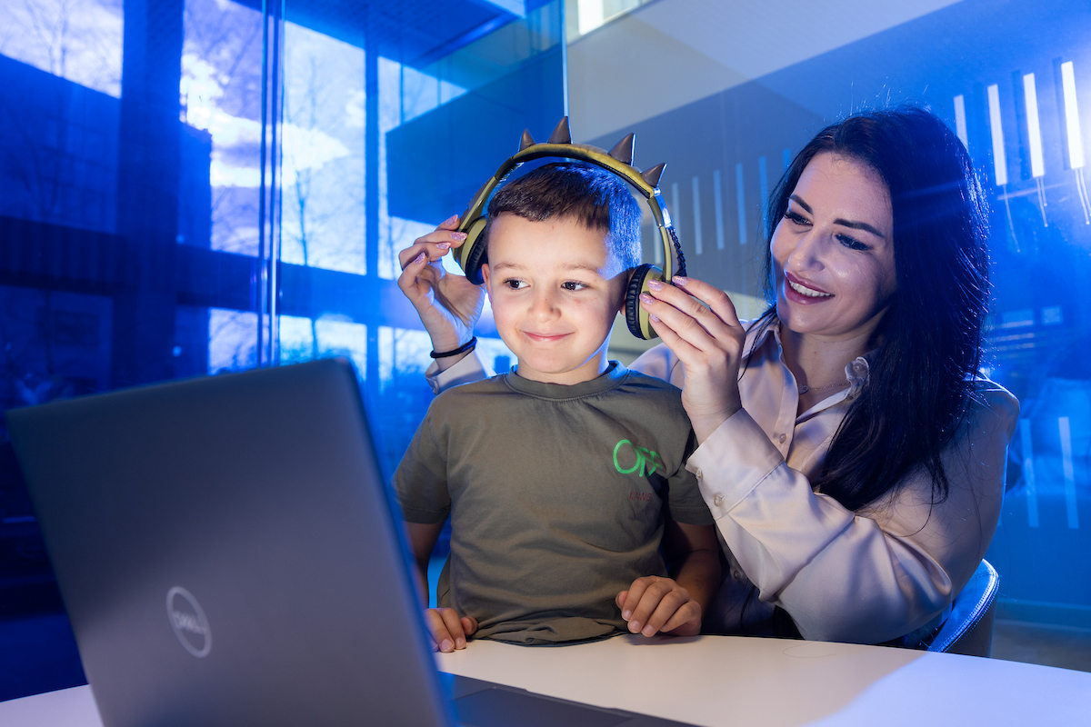 An of a woman with a child wearing headphones and looking at a laptop
