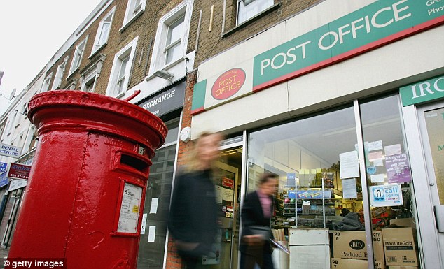 An image of a British red postbox outside a Post Office with pedestrians walking past it on the street.