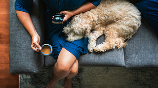 An image of a woman sitting down holding a smartphone with a dog beside her.